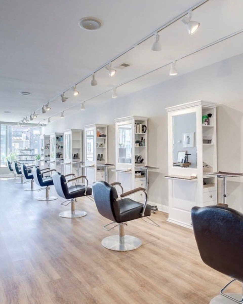 tall single-sided salon stations with full-length mirrors, drawers and shelving along one wall in a large, modern hair salon