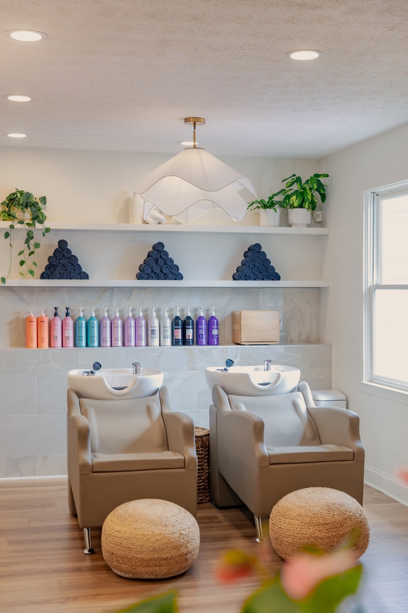 J. Italia Salon shampoo area with two shampoo stations with cushioned ottomans and recessed shelving with products and towels on the wall behind